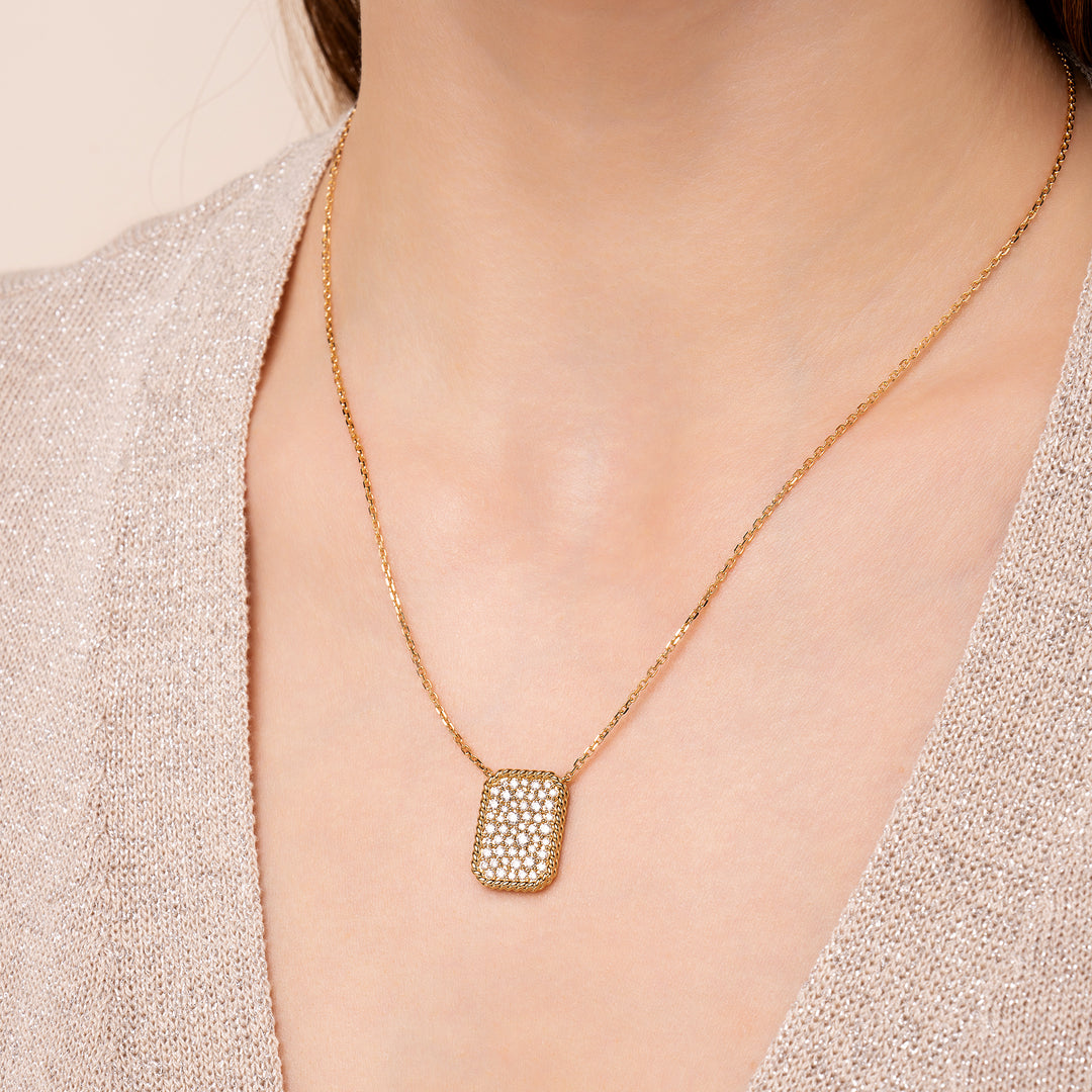A person wearing a gold necklace with a rectangular pendant adorned with diamonds.