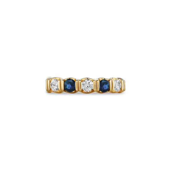 Gold ring with alternating blue and clear gemstones on a white background